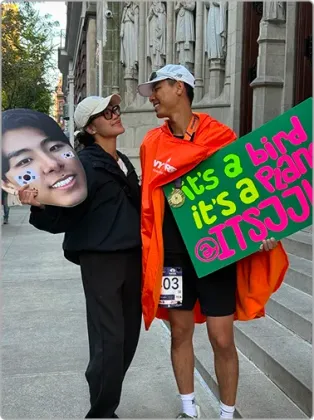 Jun Ho and a friend posing with an “it's a bird, it's a plane” finish line sign